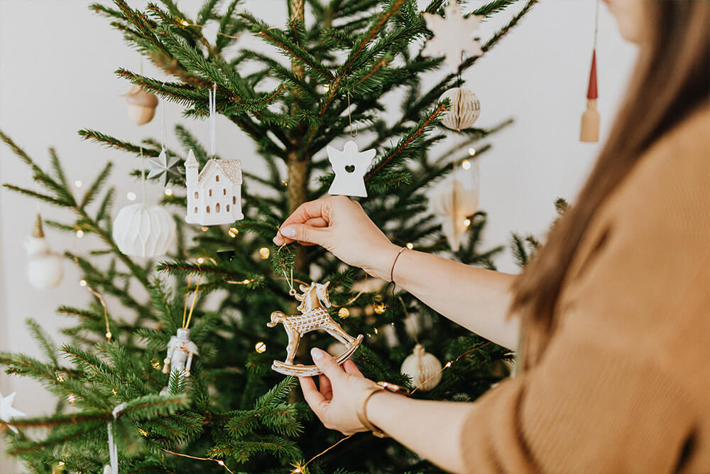 Frau hängt goldenes Schaukelpferd an den Weihnachtsbaum.